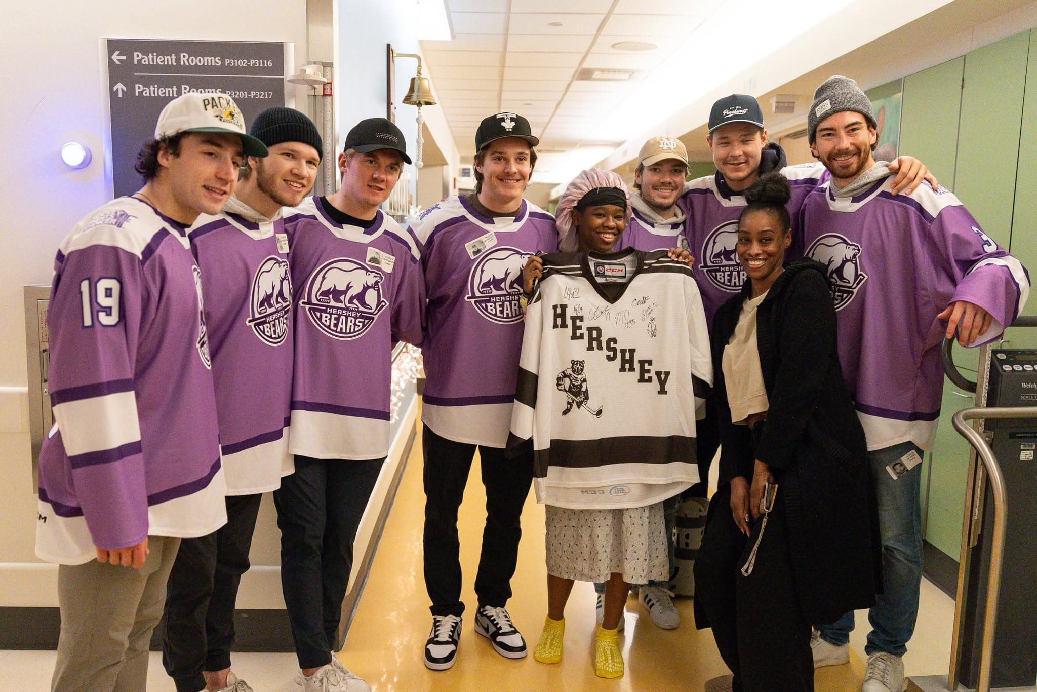 The Hershey Bears players, wearing hockey fights against cancer jersey colors, with young fans at a hospital.